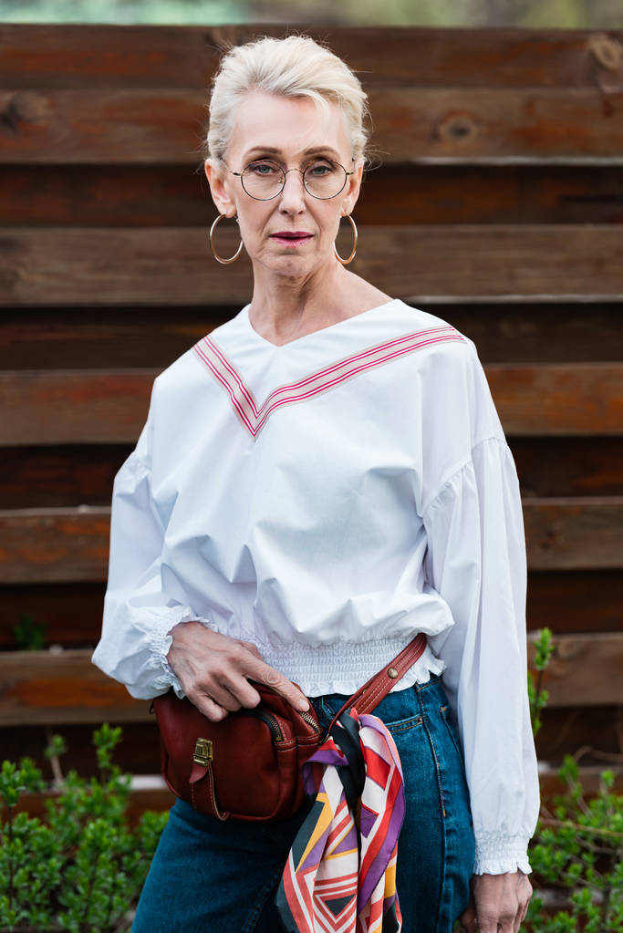 красива старша жінка позує в стильному вбранні з сумкою для талії
  - Фото, зображення