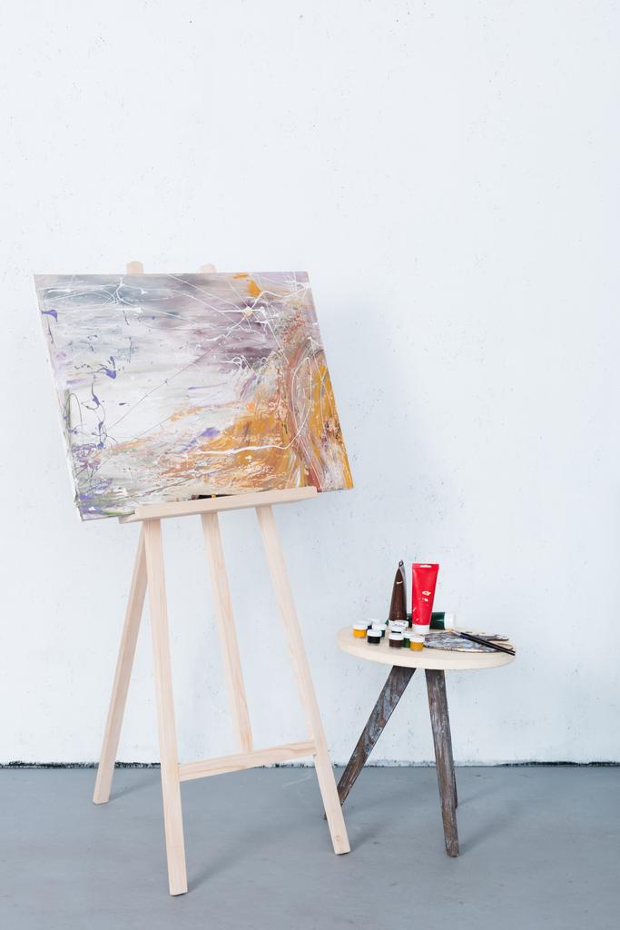 painting on easel and paints on stool in creative workshop - Photo, Image