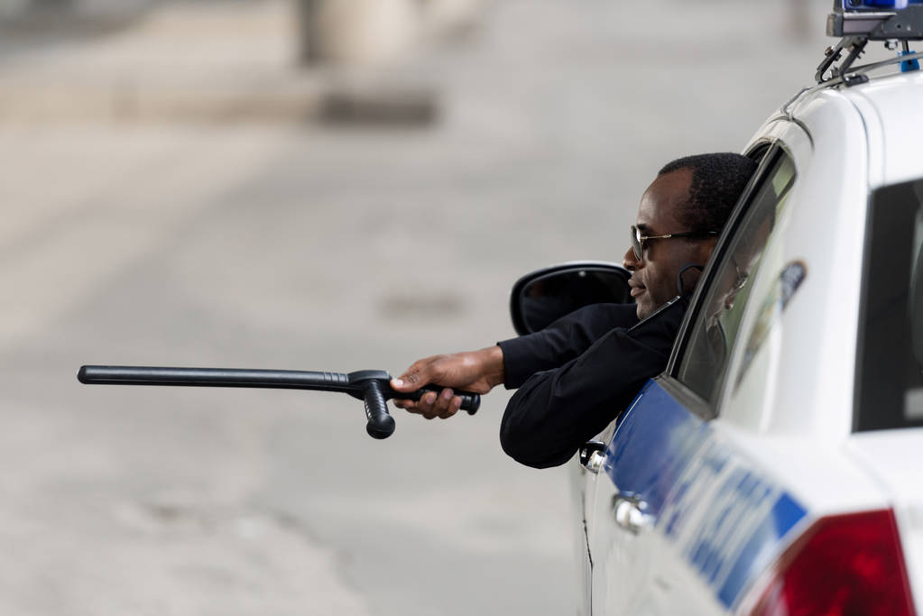 Afrikanisch-amerikanischer Polizist blickt mit Fledermaus aus Fenster von Polizeiauto - Foto, Bild