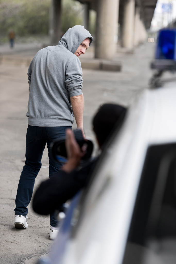 policía mirando a un joven encapuchado alejándose por la calle por la ventana
 - Foto, imagen