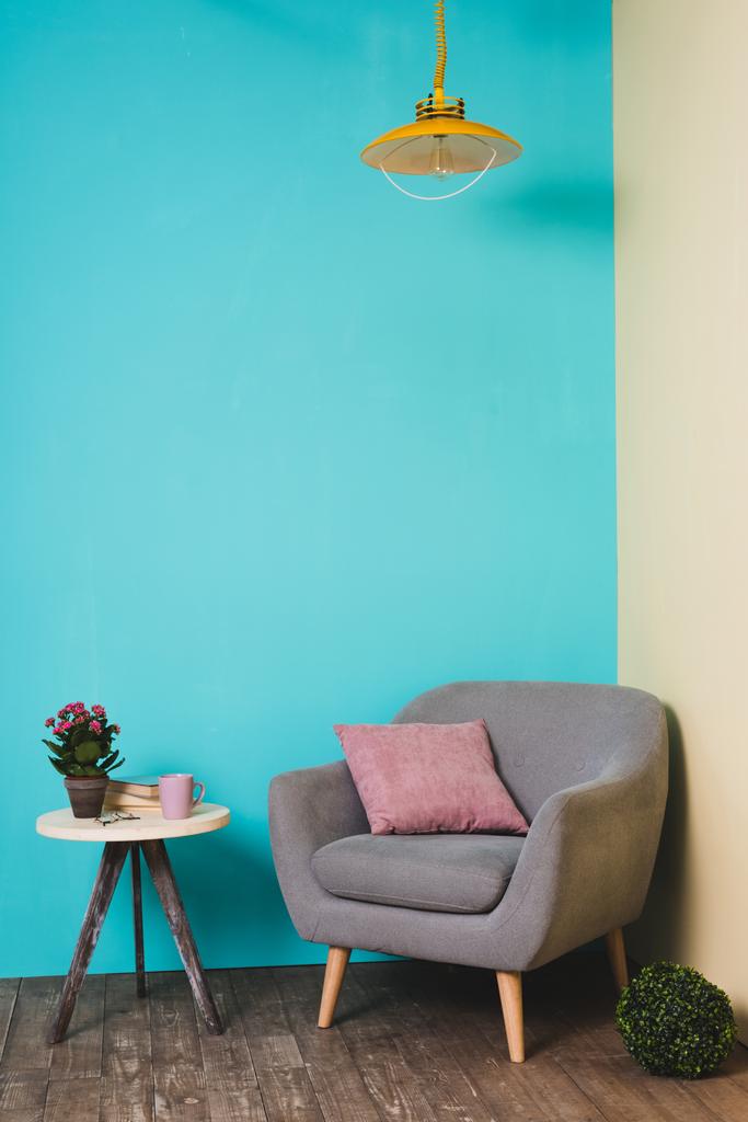 tabel met plant en fauteuil met kussen in kamer in vintage stijl - Foto, afbeelding
