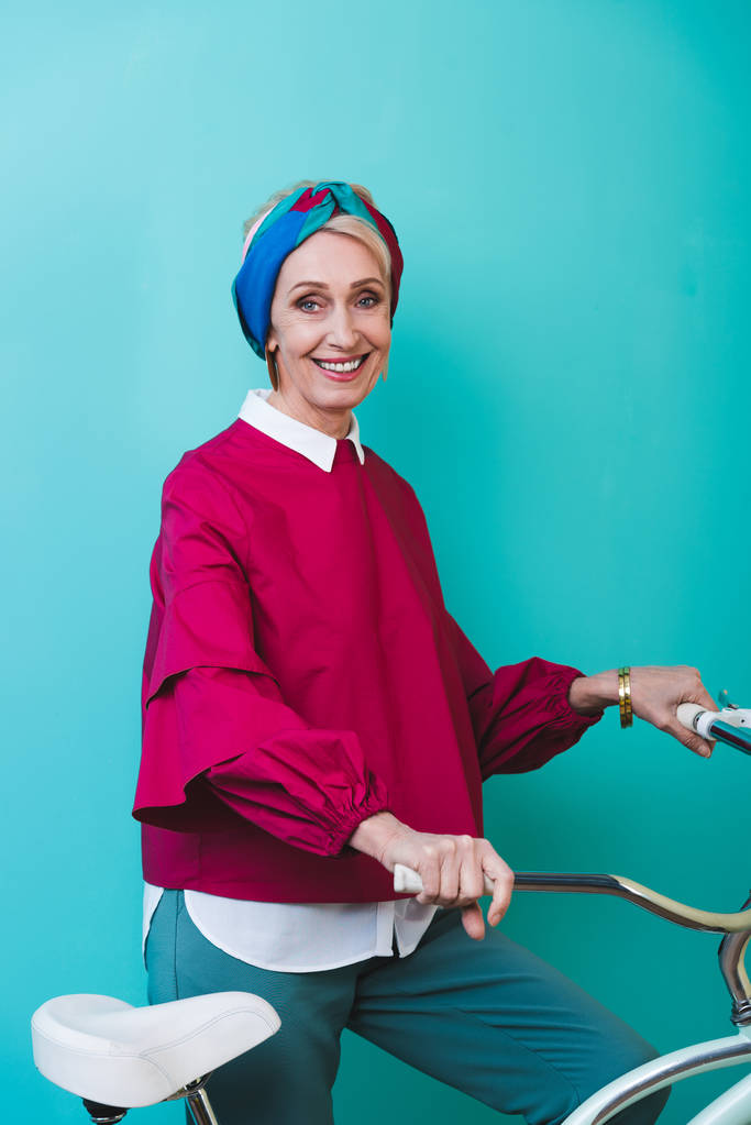 весела старша жінка, що стоїть з велосипедом, ізольована на бірюзовому
 - Фото, зображення