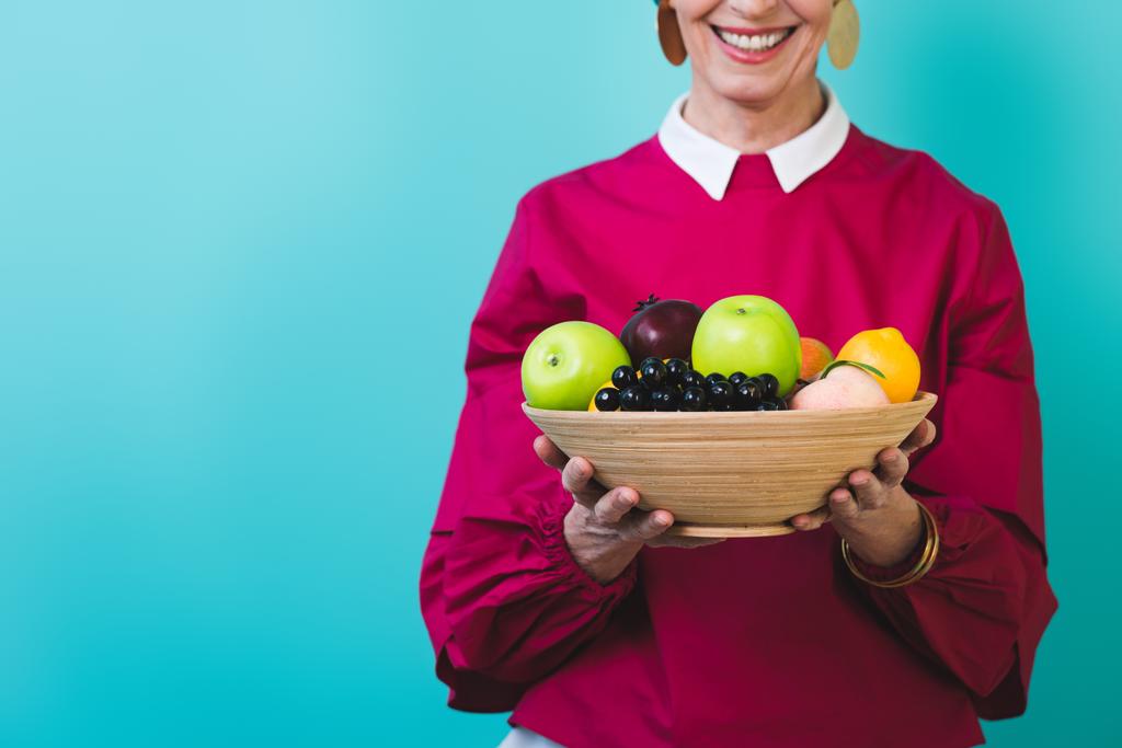 vista ritagliata della donna anziana sorridente con frutta fresca, isolata sul blu
  - Foto, immagini