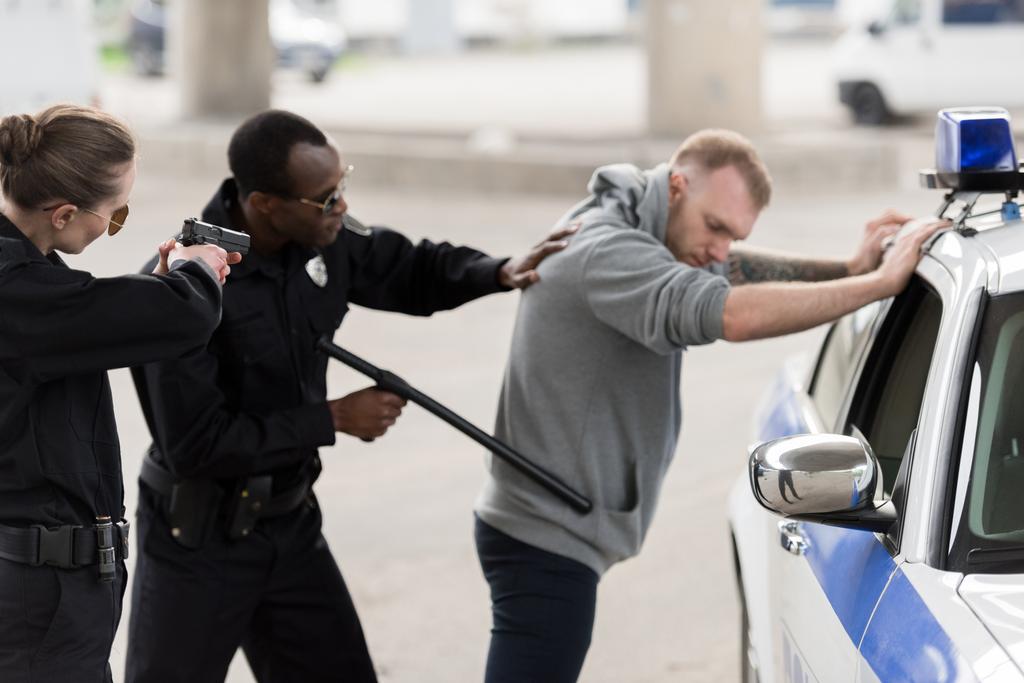 Afryki amerykański policjant zatrzymania młodego człowieka i policjantka celowania przez pistolet  - Zdjęcie, obraz