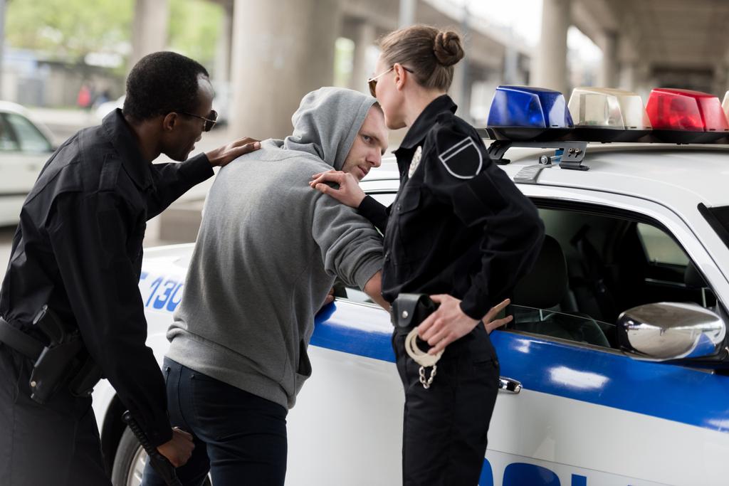 αστυνομικός και αστυνομικίνα συλλαμβάνοντας νεαρό άνδρα στα φούτερ με κουκούλα  - Φωτογραφία, εικόνα