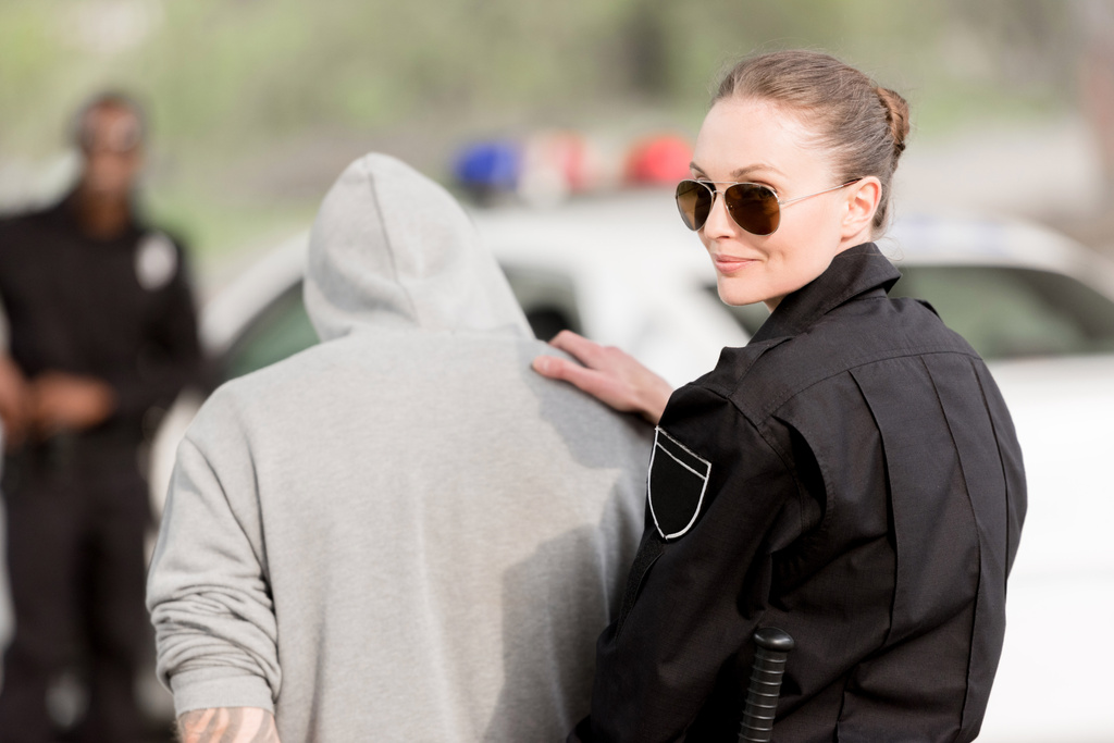 Lächelnde Polizistin mit Sonnenbrille und verhaftetem Kriminellen  - Foto, Bild