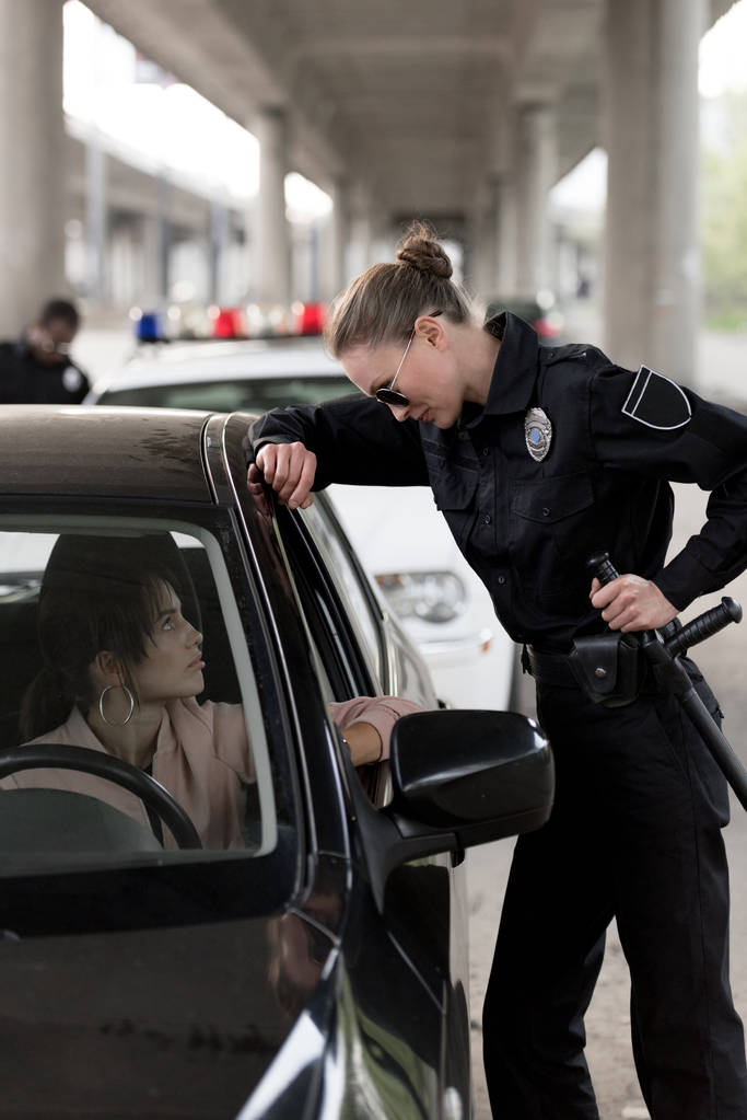 rendőrnő gazdaság gumibot, és beszél a fiatal nő ül az autó oldalnézetből  - Fotó, kép