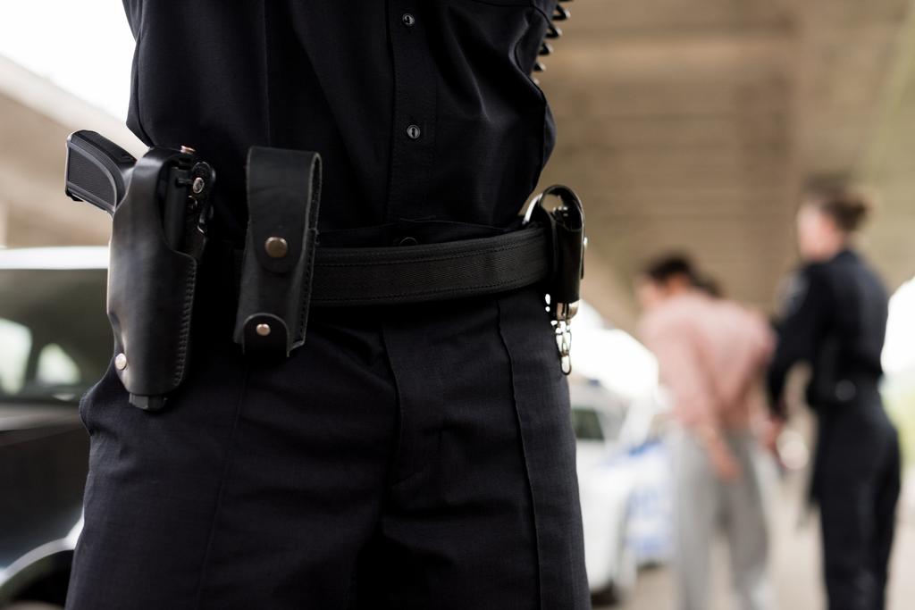 bijgesneden afbeelding van politieagent gordel met geweer en handboeien  - Foto, afbeelding