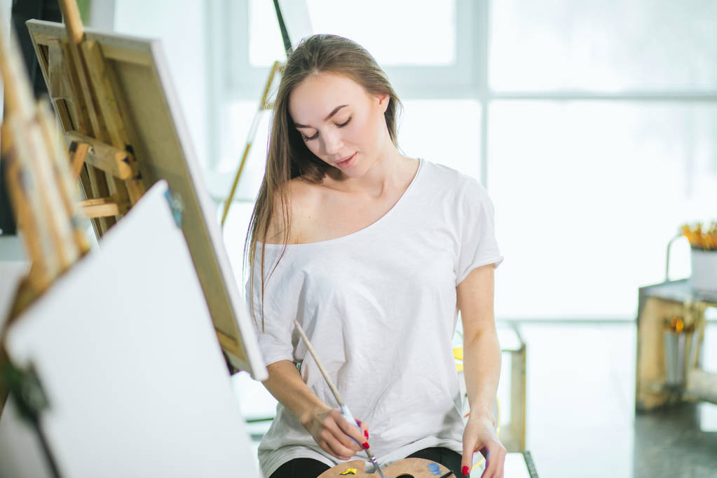 Time for creating. Attractive woman posing fullface while painting a sea-scape - Photo, Image