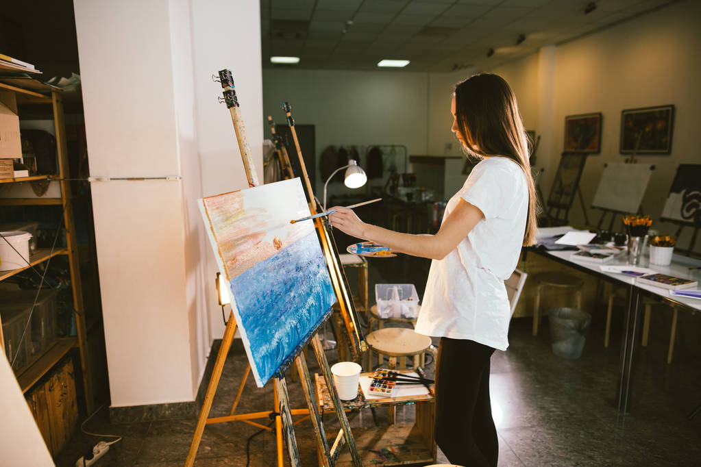 Mujer artista pintando un cuadro sobre caballete con pinturas al óleo en su taller
 - Foto, Imagen