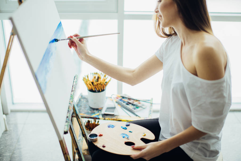 Nő művész festeni egy képet, egy jól megvilágított stúdióban - Fotó, kép