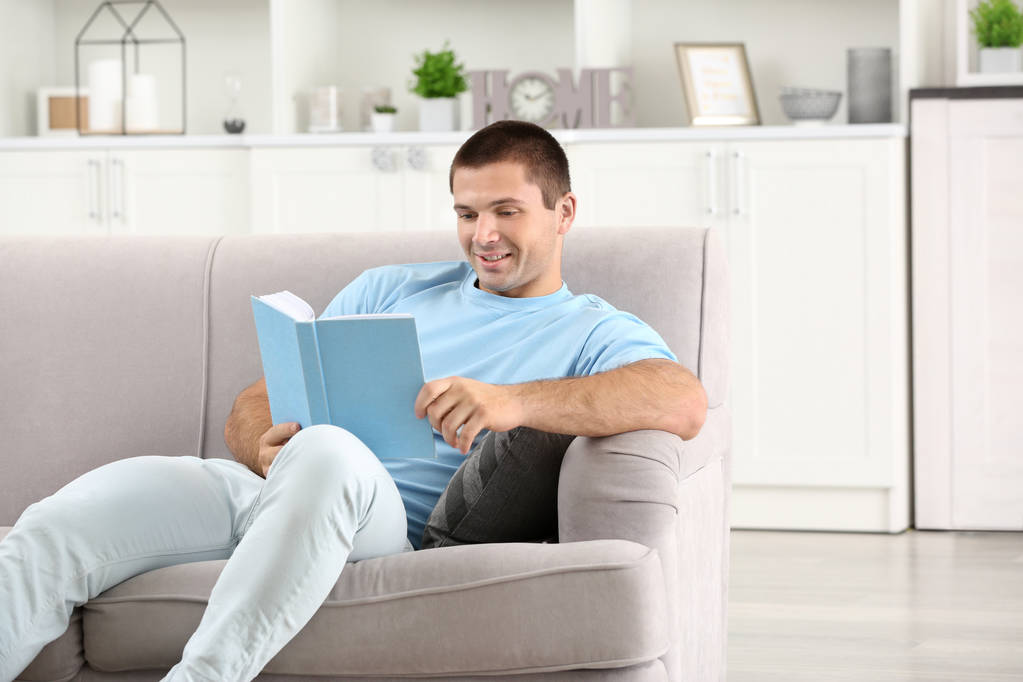 młody człowiek czyta książkę na kanapie w domu - Zdjęcie, obraz