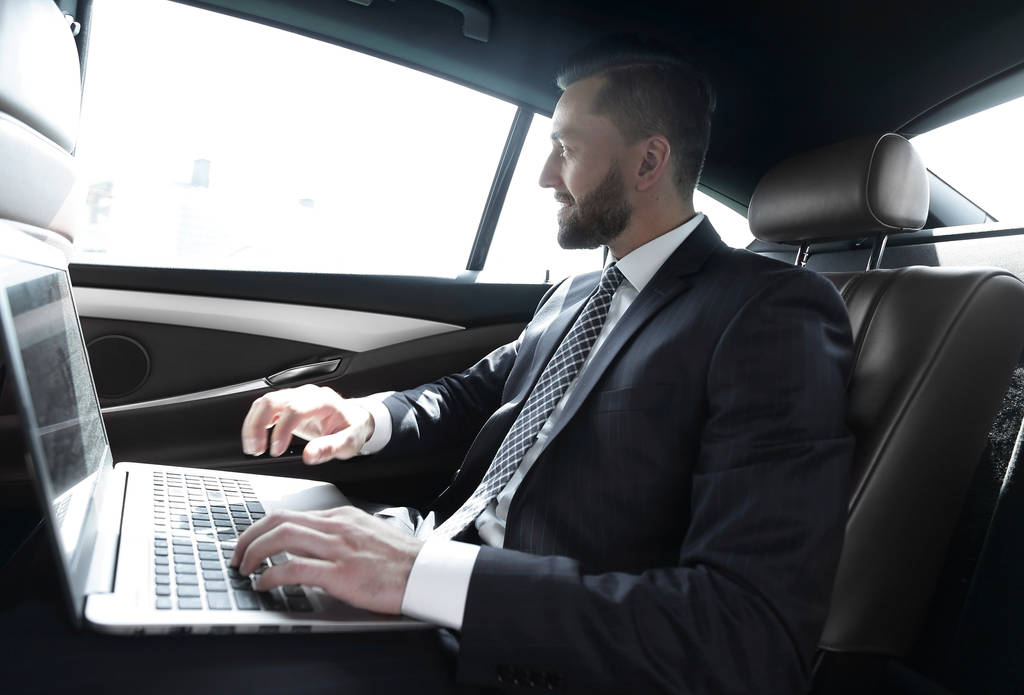 Empresario escribiendo texto en el ordenador portátil mientras está sentado en el coche
 - Foto, imagen