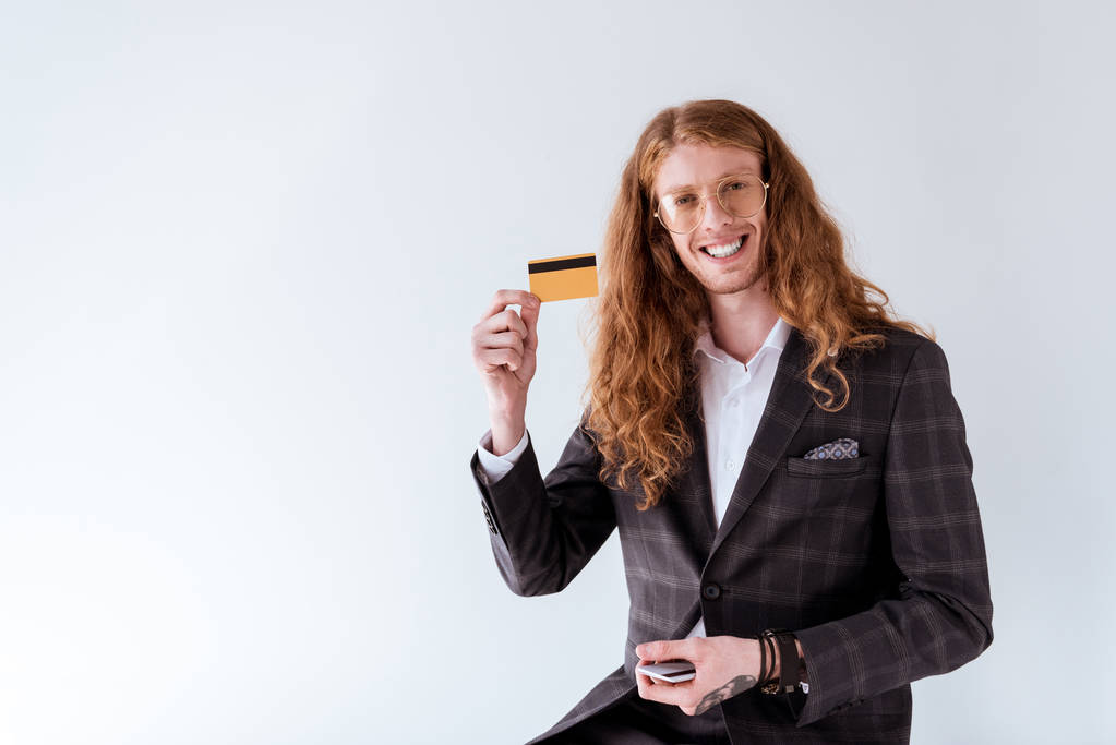 s úsměvem Tetovaný podnikatel s kudrnatými vlasy ukazuje kreditní kartu izolované na bílém - Fotografie, Obrázek