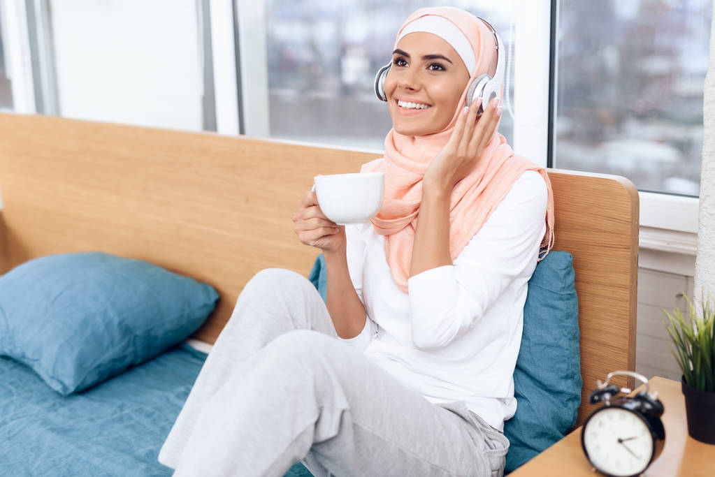 Аравійська жінка п'є чай і слухати музику, сидячи на ліжку - Фото, зображення