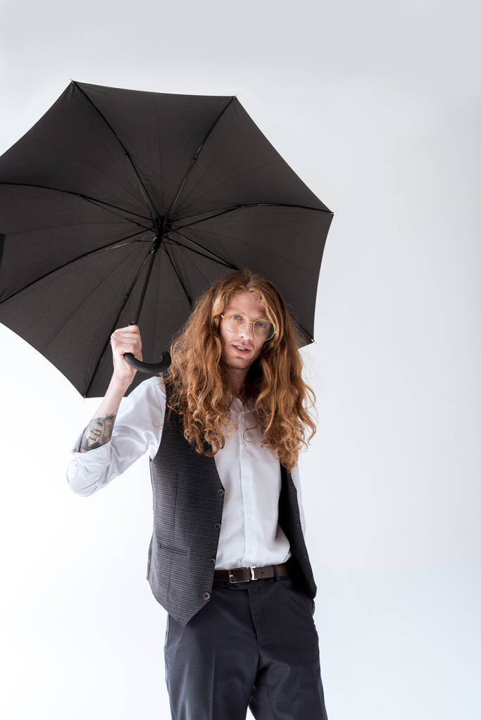 όμορφος επιχειρηματίας με σγουρά μαλλιά στέκεται κάτω από τη μαύρη ομπρέλα που απομονώνονται σε λευκό - Φωτογραφία, εικόνα