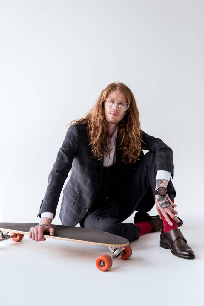 stylish businessman with curly hair sitting on floor with longboard - Photo, Image