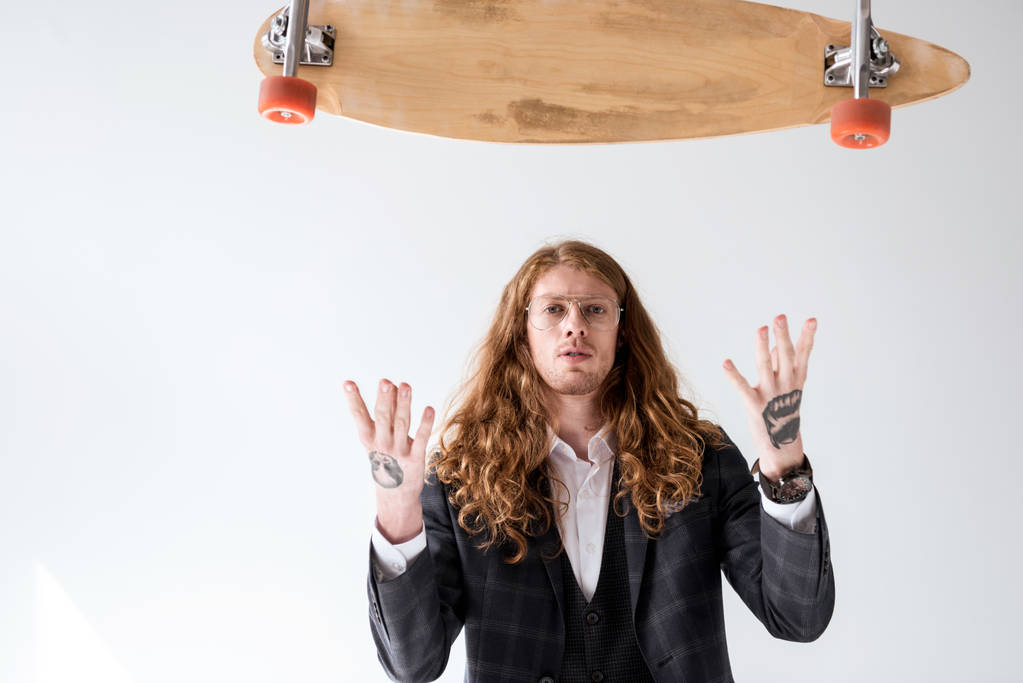 Stylový podnikatel s kudrnatými vlasy chytat padající longboard izolované na bílém - Fotografie, Obrázek