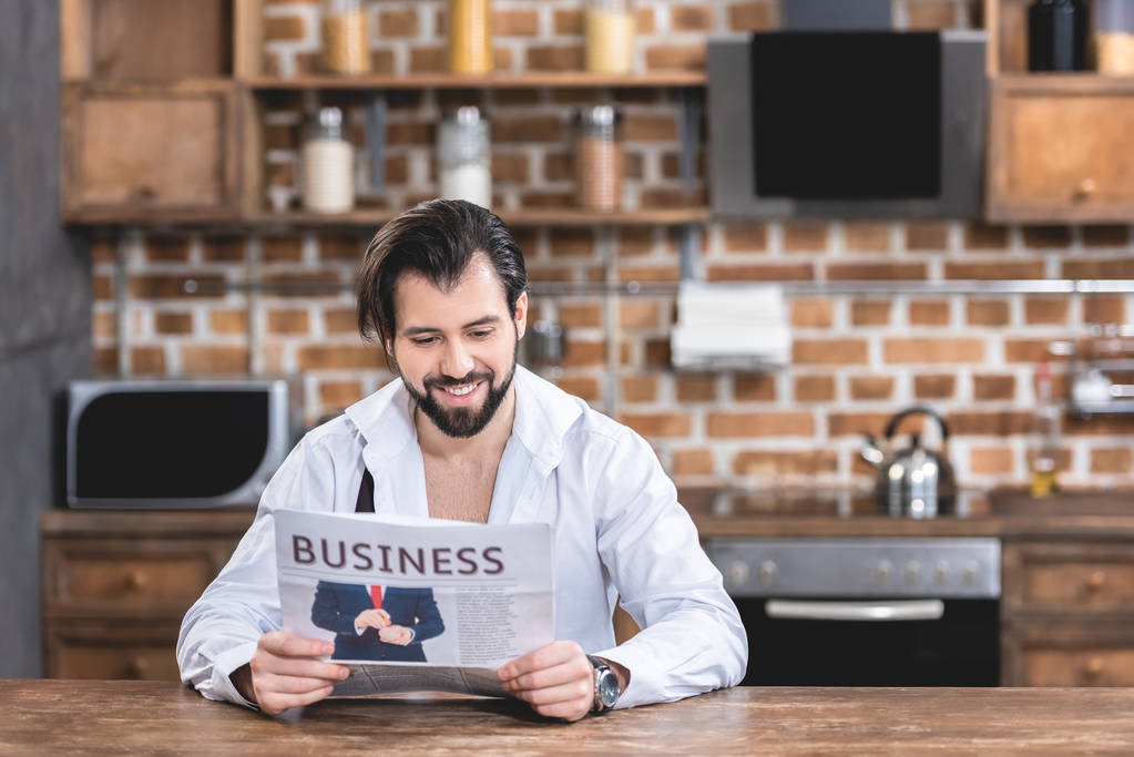 sonriente guapo solitario hombre de negocios leyendo periódico en cocina
 - Foto, imagen
