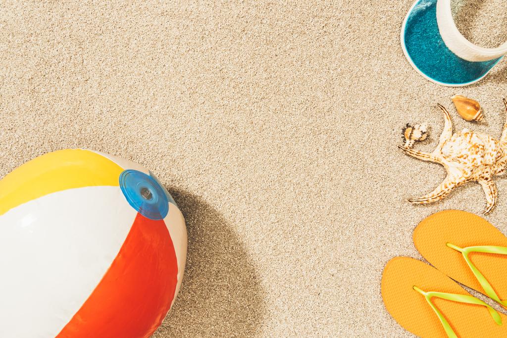 top view of arrangement of colorful beach ball, flip flops and cap on sand - Photo, Image