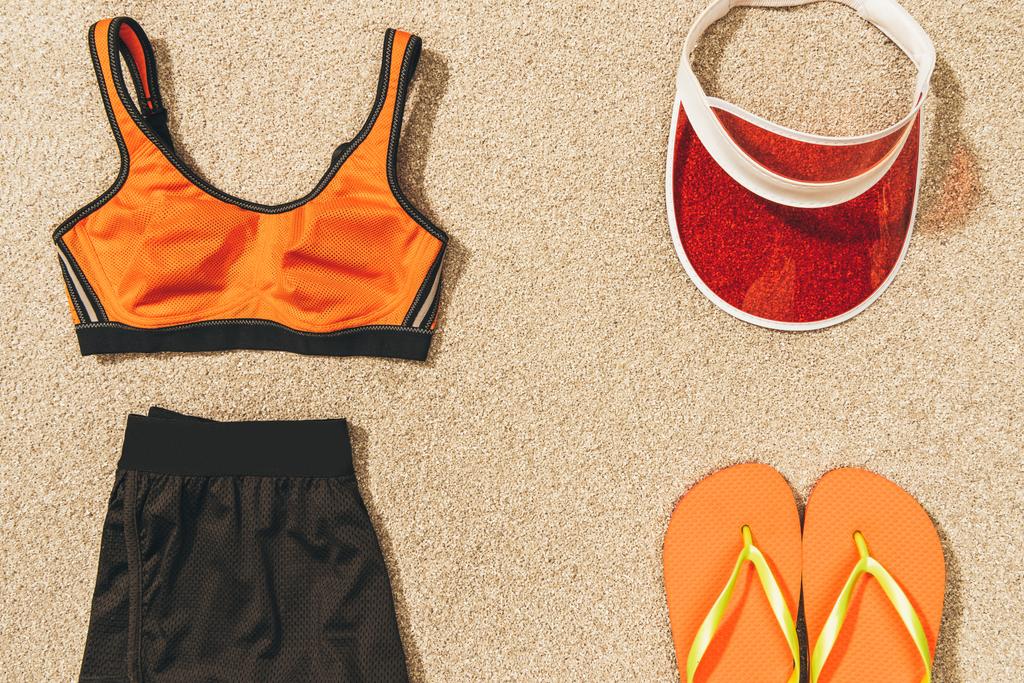 Mütze, Flip Flops und feminine Sportbekleidung auf Sand arrangiert - Foto, Bild