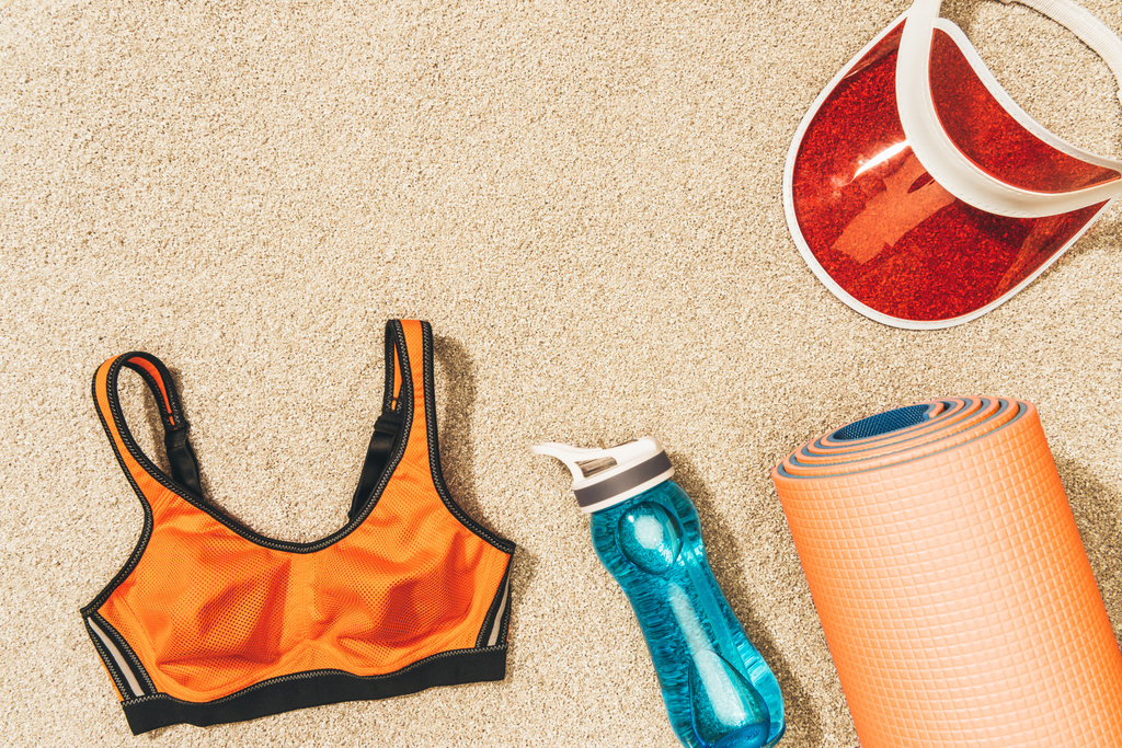 deitado plano com arranjo de tampa, sportswear feminino, tapete e garrafa de água na areia
 - Foto, Imagem