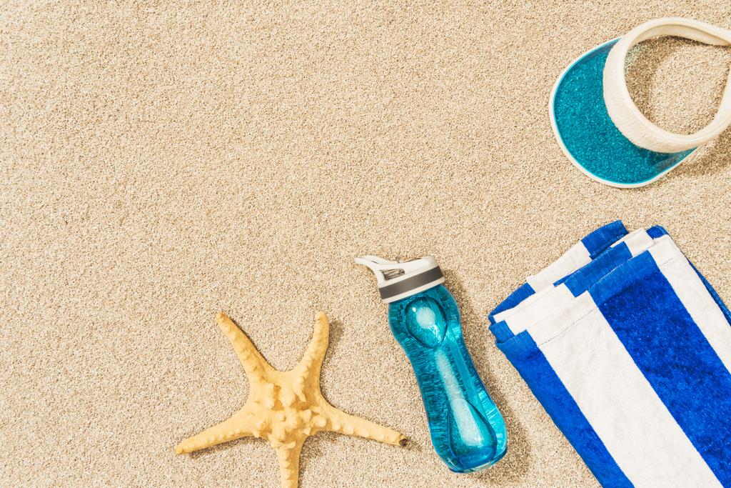 Deniz yıldızı, su şişesi, havlu ve kum üzerine düzenlenmiş kap ile düz lay - Fotoğraf, Görsel