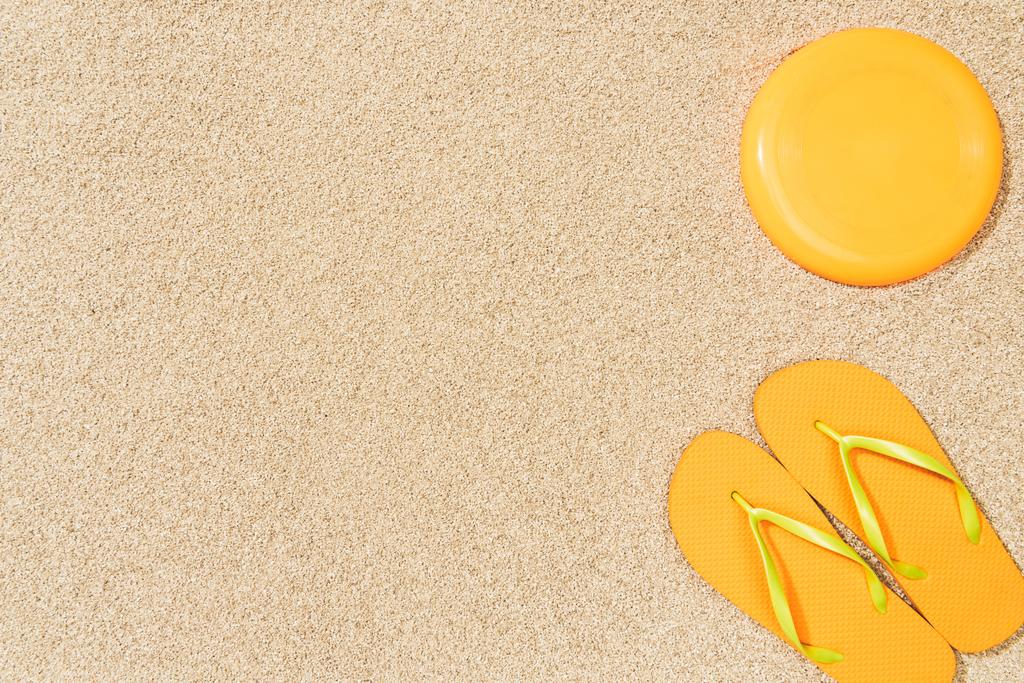 vista superior de chanclas amarillas y frisbee sobre arena
 - Foto, Imagen