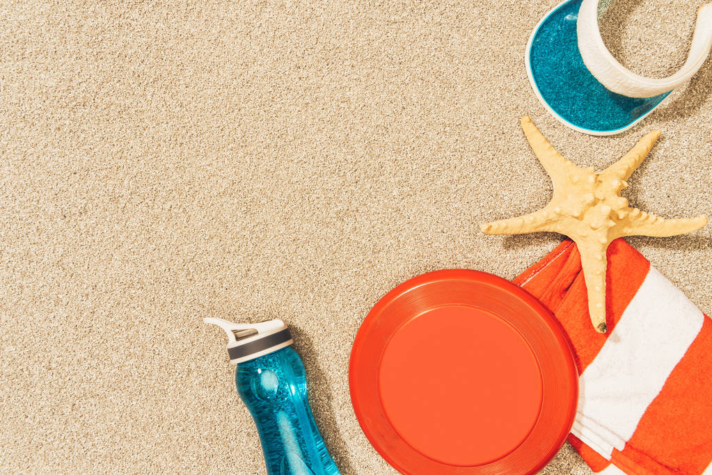 su şişesi, havlu, kap, frizbi ve deniz yıldızı kum üzerinde düz lay - Fotoğraf, Görsel