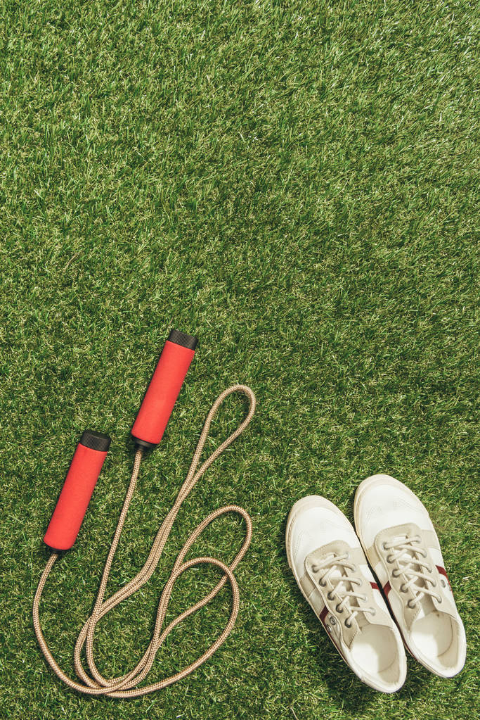 верхний вид устроенных кроссовок и скакалка на зеленой траве
 - Фото, изображение