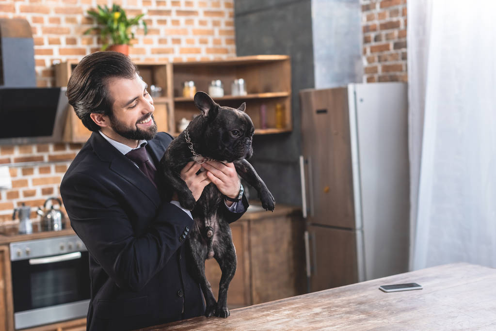 onnellinen komea yksinäinen liikemies halaus bulldog keittiössä
 - Valokuva, kuva