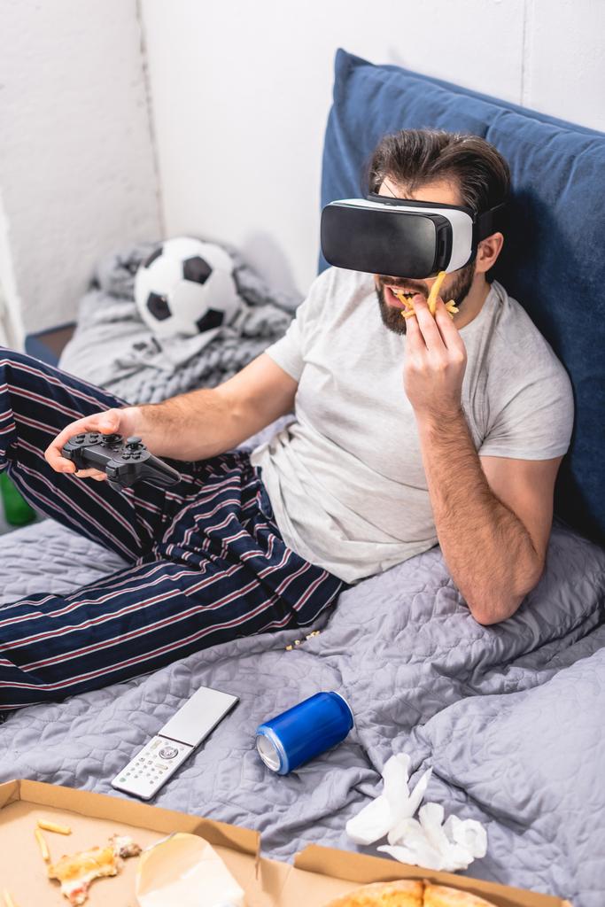 solitario utilizzando cuffie realtà virtuale, giocare al videogioco e mangiare patatine fritte in camera da letto
 - Foto, immagini