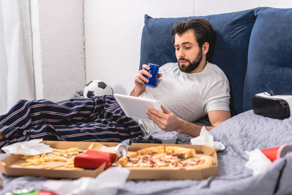 handsome loner using tablet and holding drink on bed in bedroom - Photo, Image