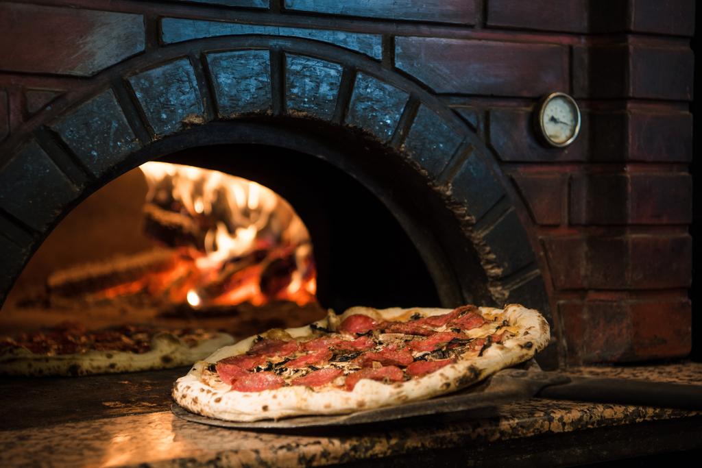 close up view of cooking process of raw pizza on wooden stove in brick oven - Photo, Image