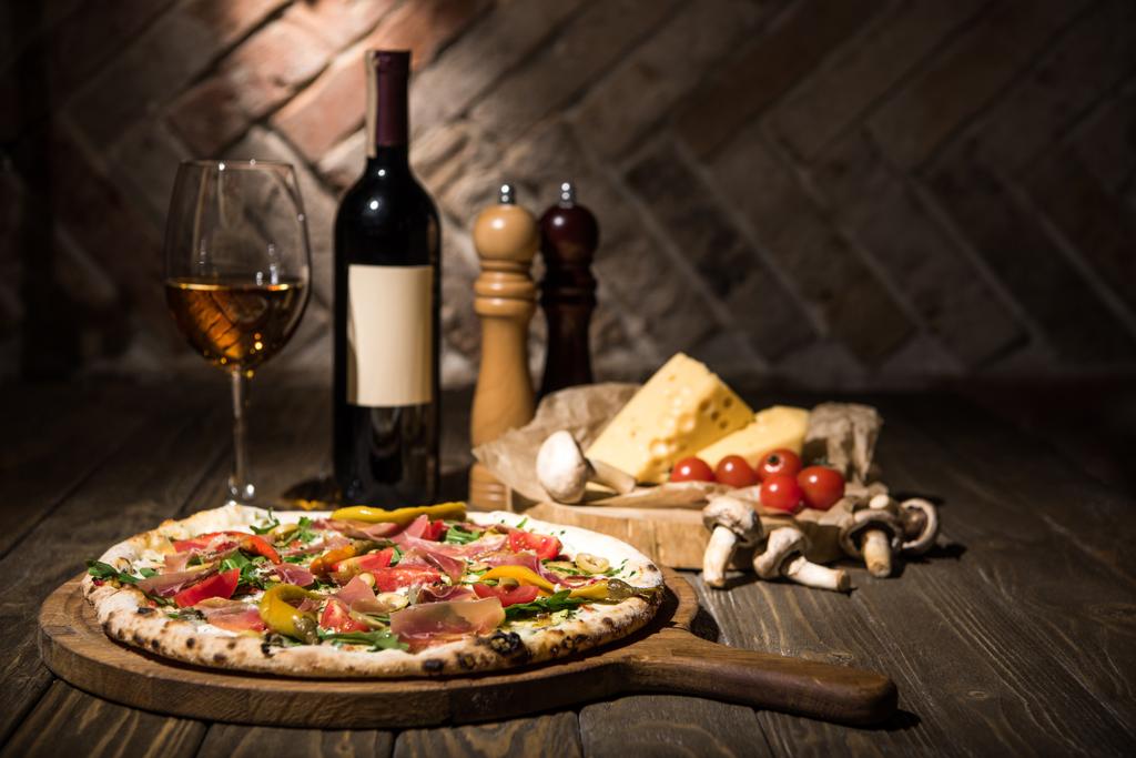 Selektywny fokus włoskiej pizzy, przyprawy, ser, pomidory cherry i butelkę wina na powierzchni drewnianych - Zdjęcie, obraz