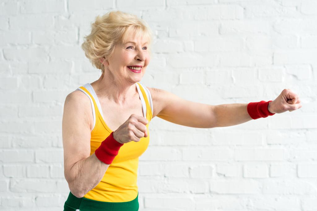 Glückliche Seniorin in Sportbekleidung boxt und schaut weg - Foto, Bild