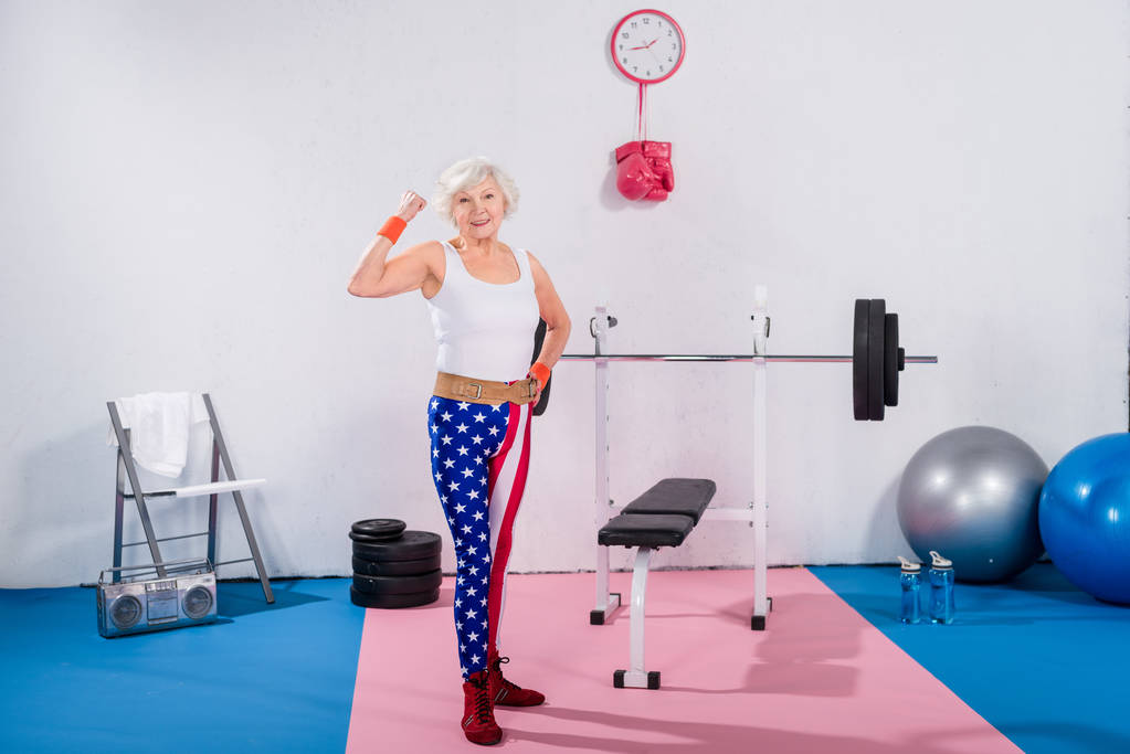 deportivo señora mayor en patriótica ropa deportiva mostrando los músculos y sonriendo a la cámara
 - Foto, imagen