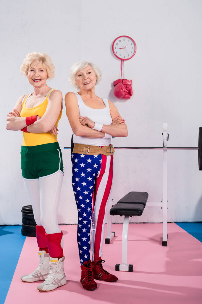 sporty senior women standing with crossed arms and smiling at camera in gym  - Photo, Image