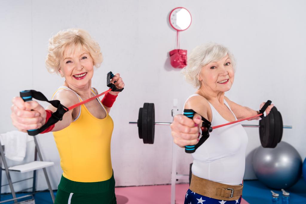 deportivo señoras mayores ejercitando con bandas de resistencia y sonriendo a la cámara
 - Foto, imagen