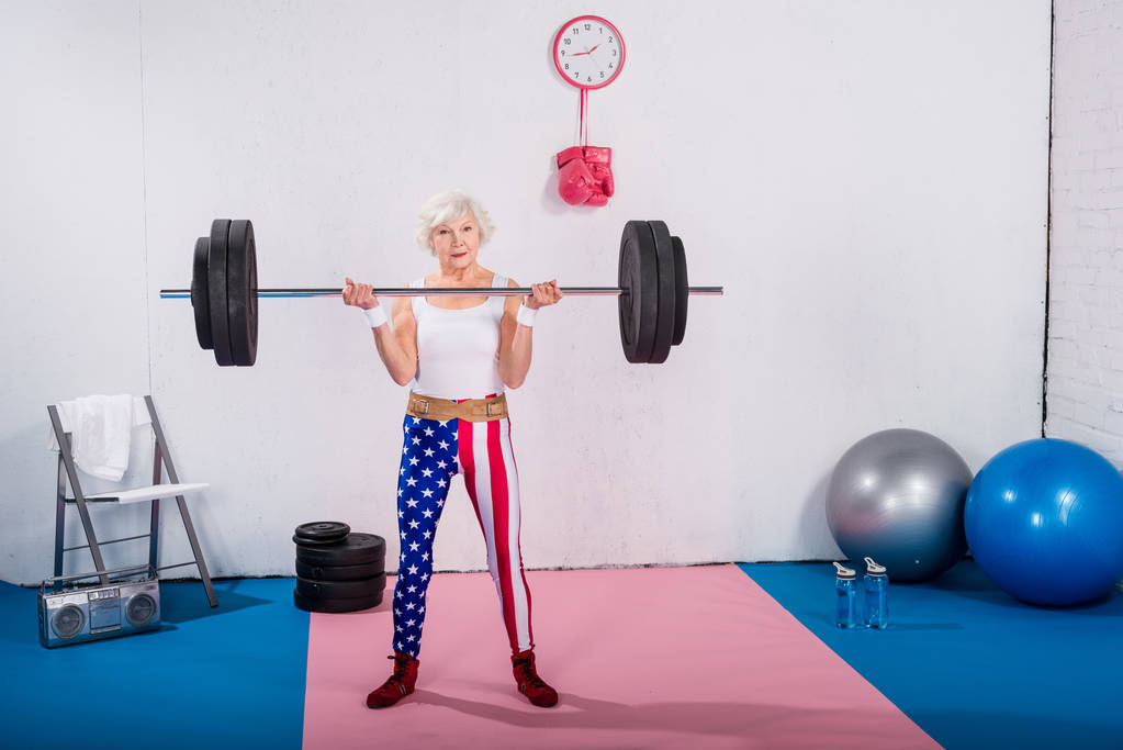 sporty senior lady lifting barbell and looking at camera  - Photo, Image