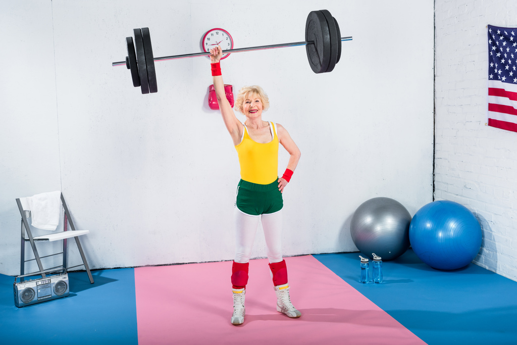 high angle view of senior sportswoman lifting barbell and smiling at camera - Photo, Image