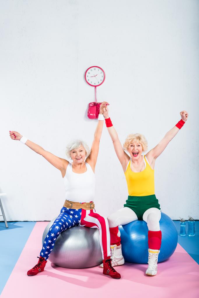 animado sênior sportswomen sentado em bolas de fitness e sorrindo para a câmera
  - Foto, Imagem
