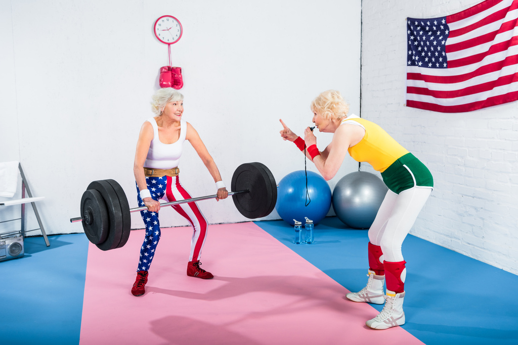 femme âgée sportive siffler et regarder la femme sportive âgée lever haltère dans la salle de gym
 - Photo, image