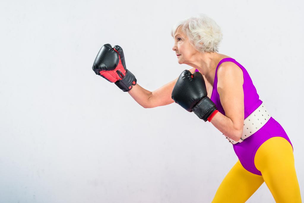 Вид сбоку спортивной пожилой дамы в боксе, изолированной на сером
 - Фото, изображение