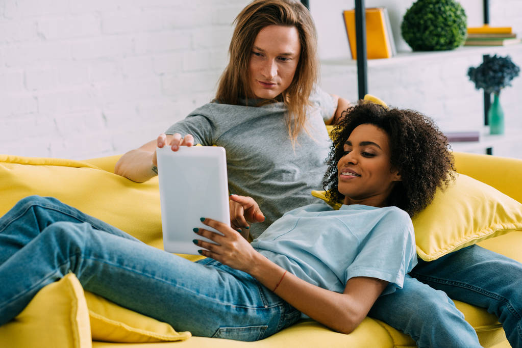 Junges multiethnisches Paar nutzt digitales Tablet auf dem Sofa - Foto, Bild
