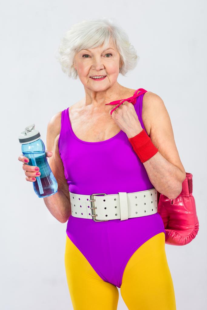 bela sportswoman sênior sorridente segurando garrafa de água e luvas de boxe
 - Foto, Imagem