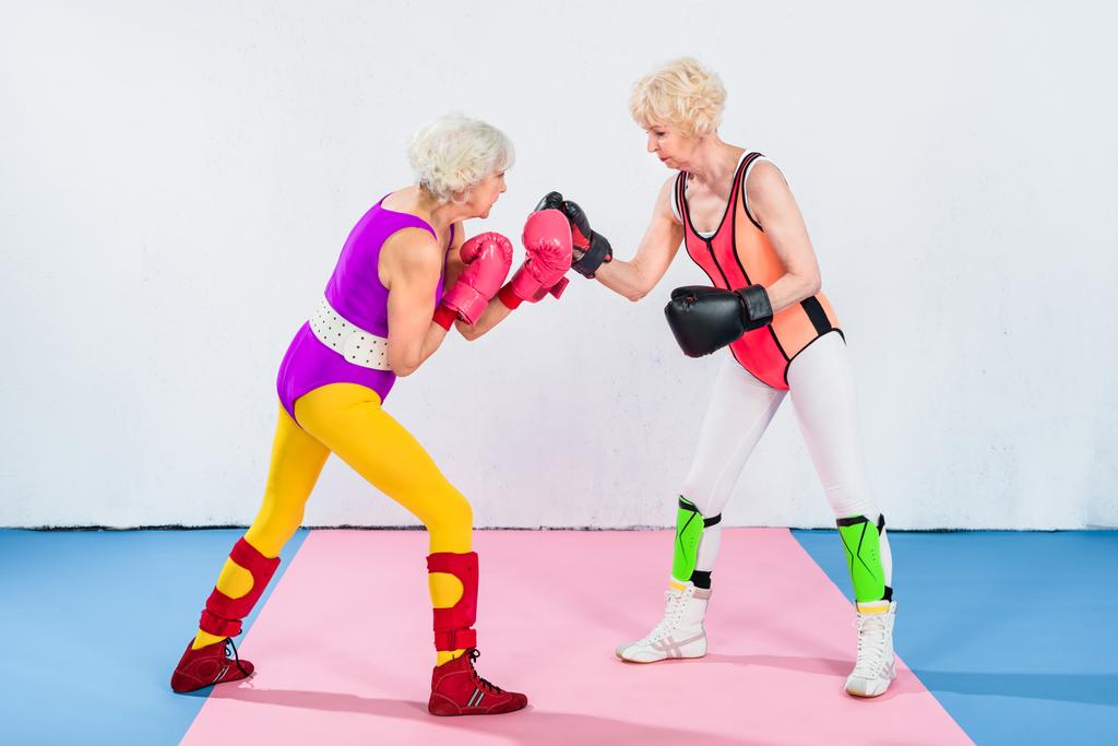 side view of senior sportswomen in boxing gloves fighting and looking at each other - Photo, Image