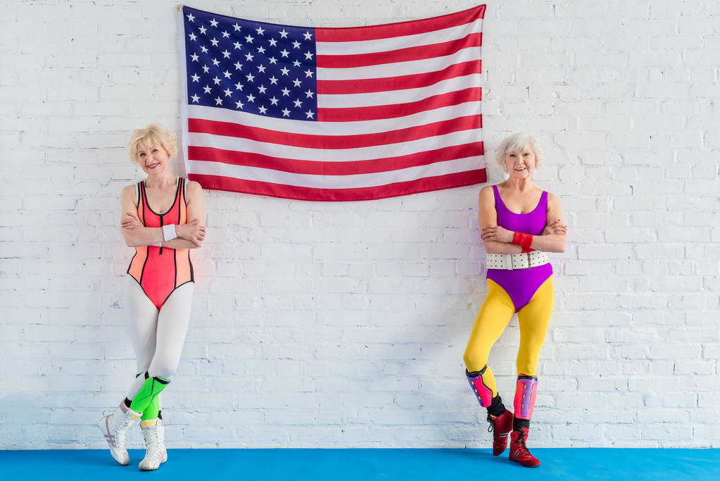 belles sportives seniors debout avec les bras croisés près du drapeau américain et souriant à la caméra
  - Photo, image