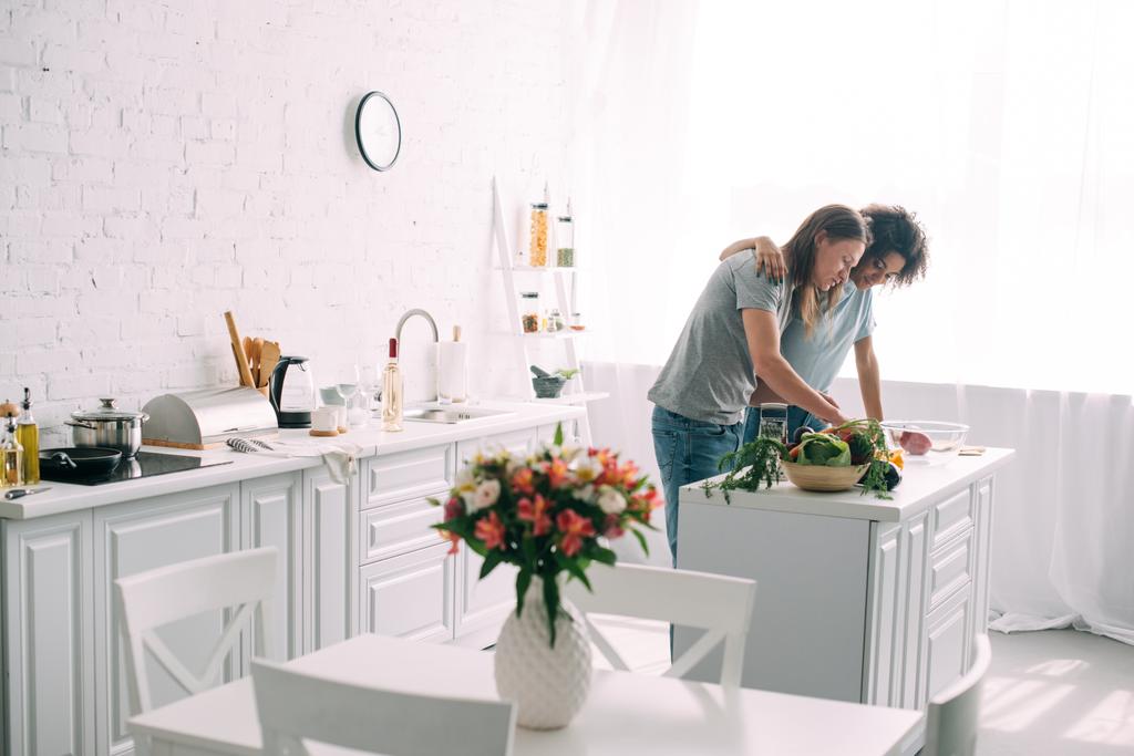 čelní pohled mladé afroamerické ženy všeobjímající přítel, zatímco on vaření v kuchyni  - Fotografie, Obrázek
