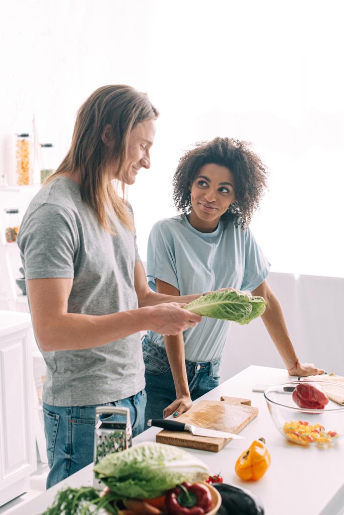 jovem casal multiétnico de pé na cozinha com folhas de salada
  - Foto, Imagem